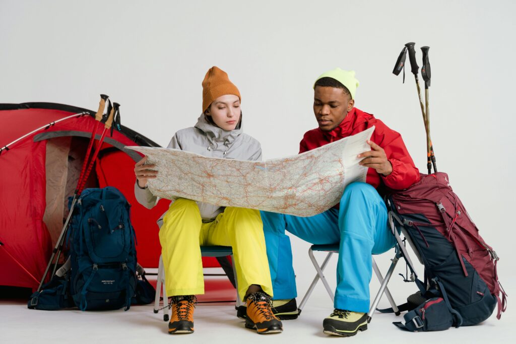 pexels-photo-7009599-7009599 Two young hikers study a map, preparing for a winter trek with camping gear and equipment.